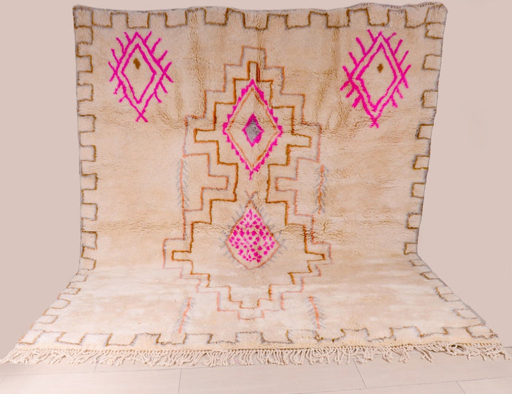 Detail shot of a beige and pink Beni Ourain rug featuring geometric patterns and fringe edges.