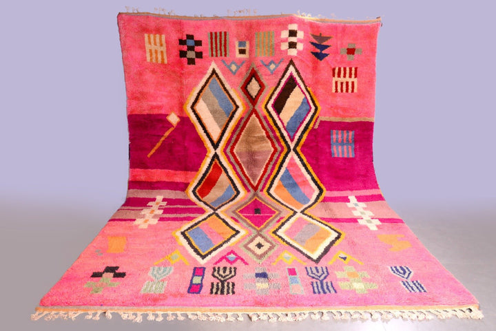 Lifestyle shot of a pink Moroccan rug featuring geometric patterns and fringe edges.