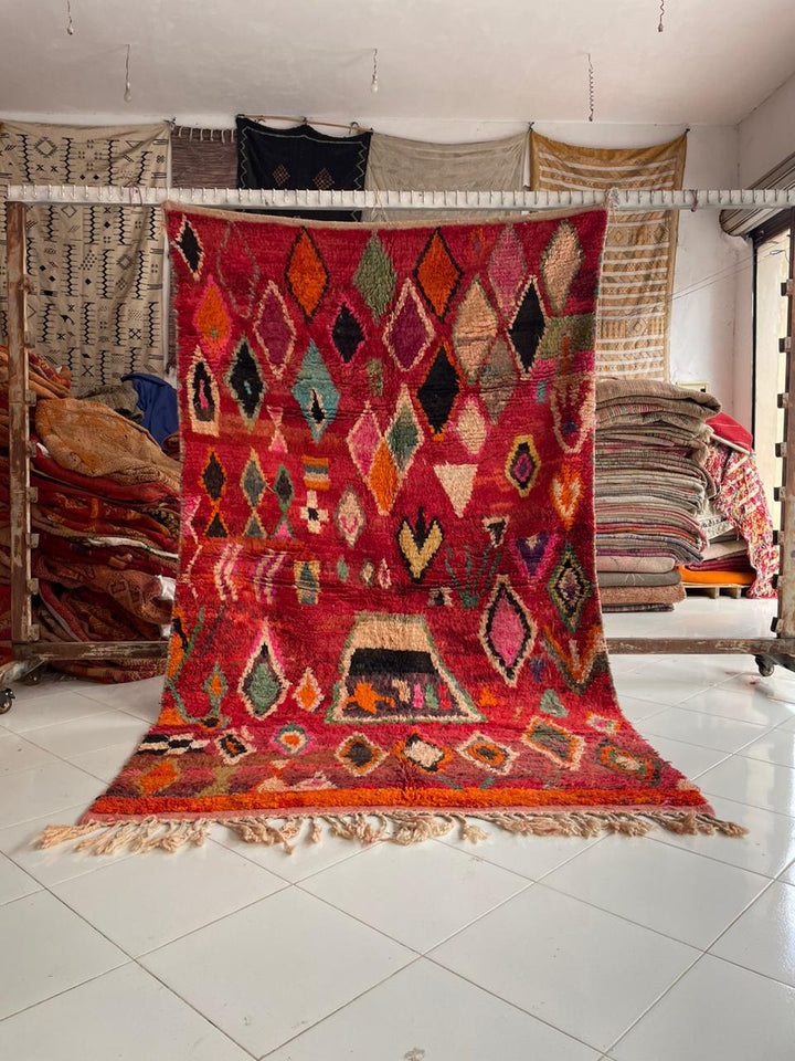 Lifestyle shot of a vintage Moroccan rug featuring geometric patterns in red, orange, and green.
