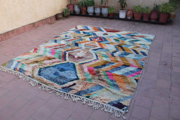Lifestyle shot of a colorful Moroccan rug featuring geometric patterns and fringed edges.
