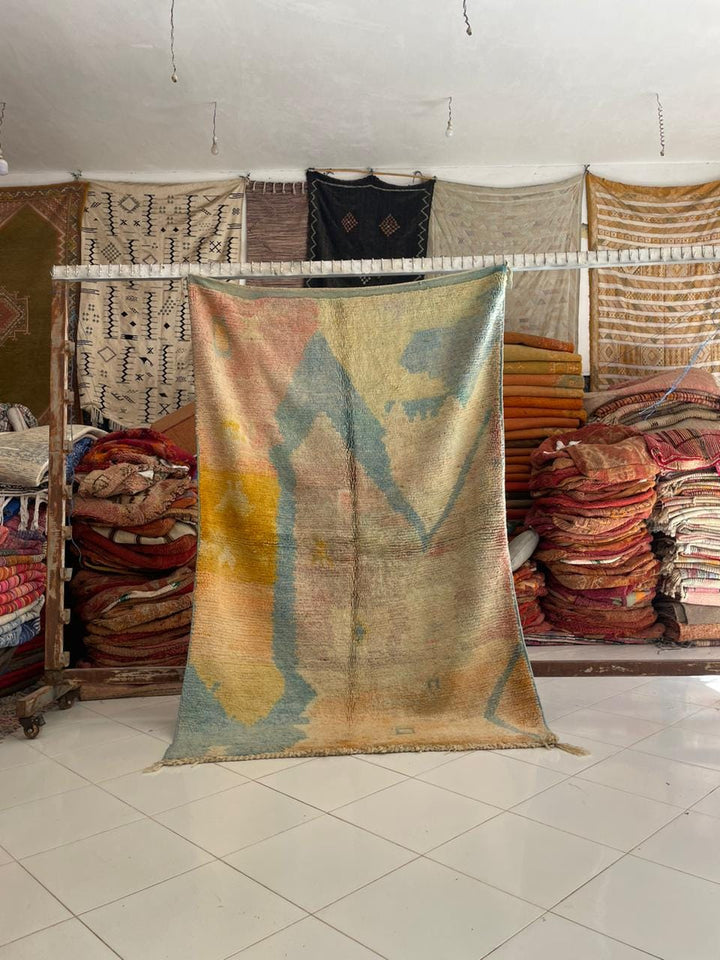 Lifestyle shot of a faded vintage Moroccan rug featuring tribal patterns in blue, orange, and yellow.