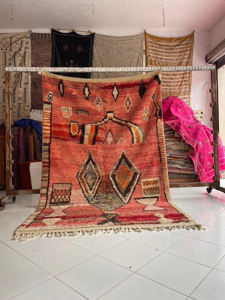Lifestyle shot of a faded red tribal Boujaad rug with fringe edges on a natural background.