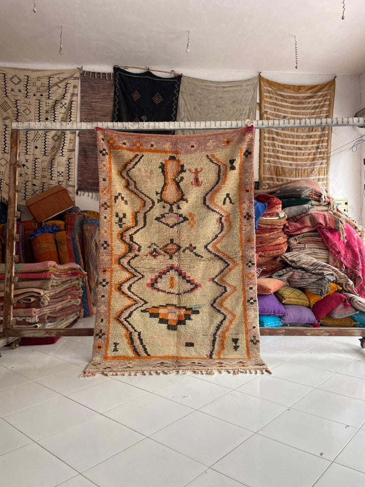 Lifestyle shot of a vintage Moroccan rug featuring geometric patterns in beige and orange.