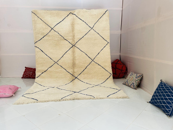 Lifestyle shot of a beige and blue Moroccan Berber rug with a diamond pattern in a studio setting.