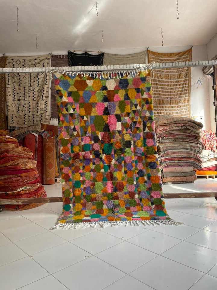 Lifestyle shot of a colorful Moroccan rug featuring geometric patterns and fringe edges.