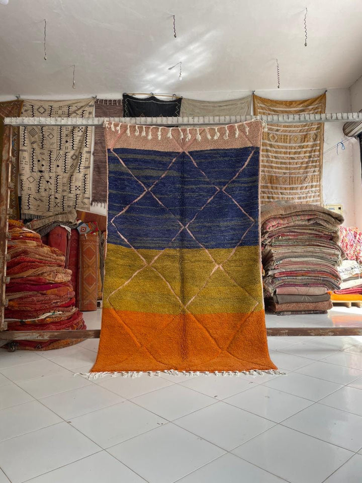 Lifestyle shot of a colorful Moroccan rug with geometric patterns in blue, yellow, and orange.