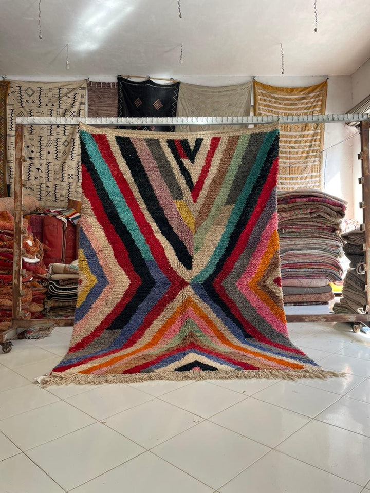 Lifestyle shot of a colorful Moroccan rug featuring geometric patterns in red, blue, yellow, and black.