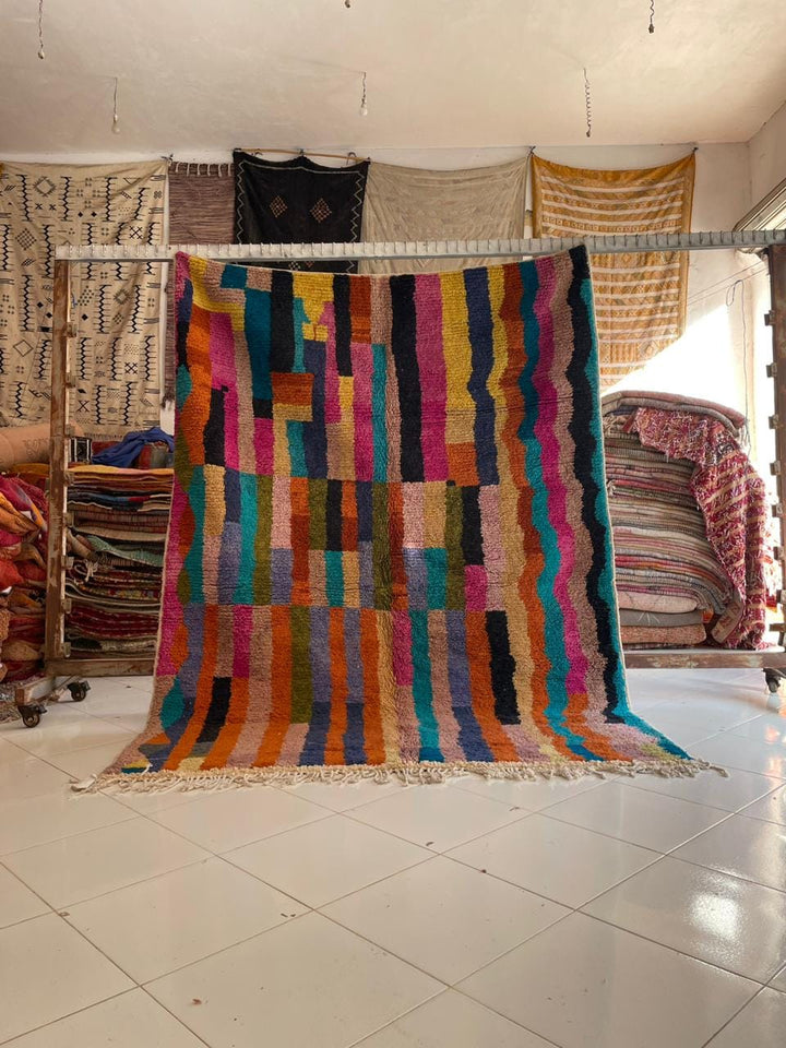 Lifestyle shot of a colorful Moroccan rug with a striped pattern in pink, blue, and green.