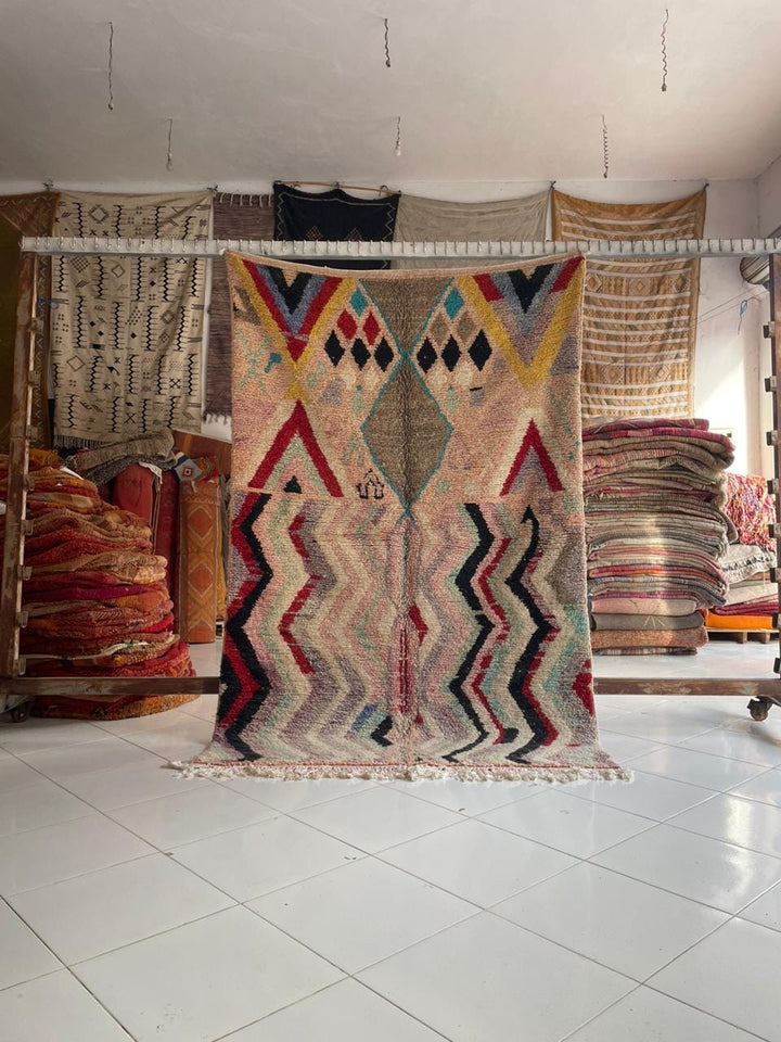 Lifestyle shot of a colorful Moroccan rug with zigzag pattern and fringe edges on a natural background.