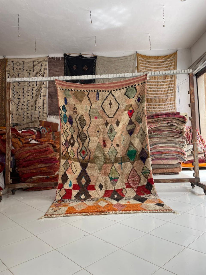 Lifestyle shot of a colorful Moroccan rug featuring beige, red, green, and orange tones.