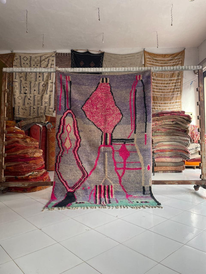 Lifestyle shot of a pink Moroccan rug with tribal patterns and fringed edges.