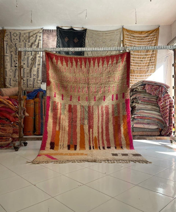Lifestyle shot of a colorful Moroccan rug with red, orange, and pink tones in a natural setting.