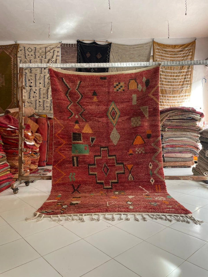 Lifestyle shot of a red Moroccan rug with green and orange accents in a natural setting.