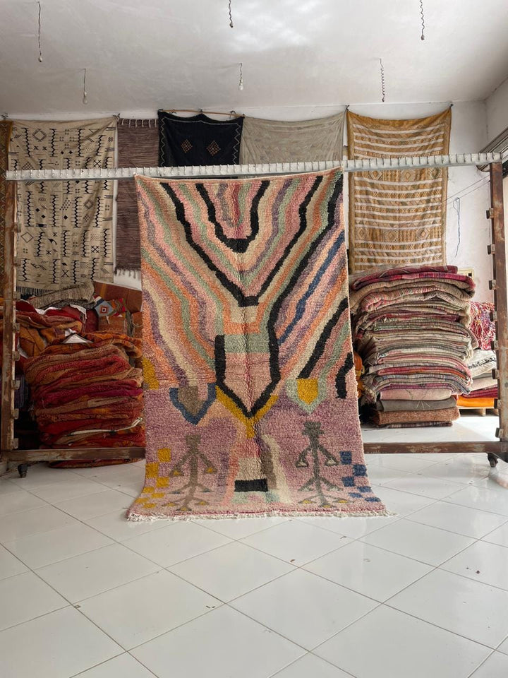 Lifestyle shot of a colorful Moroccan rug featuring geometric patterns and fringe edges.