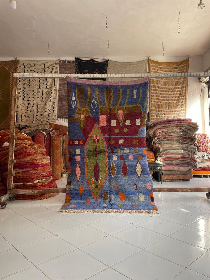 Lifestyle shot of a colorful Moroccan rug featuring geometric patterns and fringe edges.