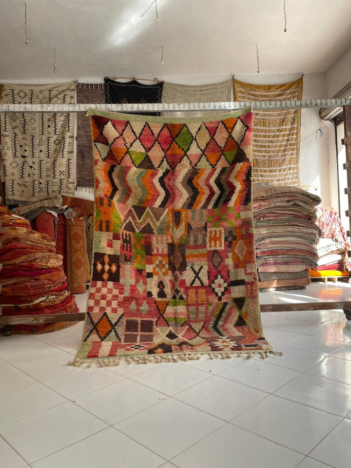 Lifestyle shot of a colorful Moroccan rug featuring geometric patterns and fringe edges.
