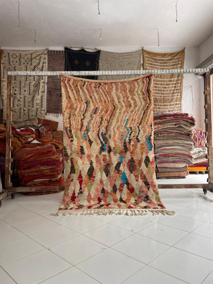Lifestyle shot of a colorful Moroccan rug featuring red, blue, and beige tones with fringe edges.