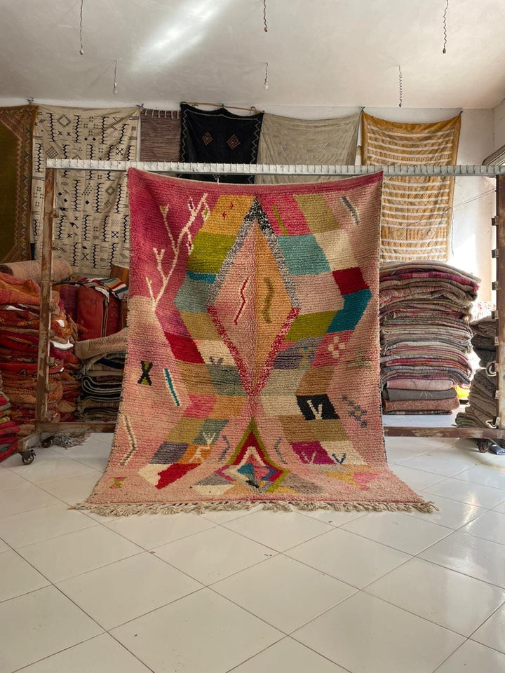 Lifestyle shot of a colorful Moroccan rug with geometric patterns in pink, blue, and green.