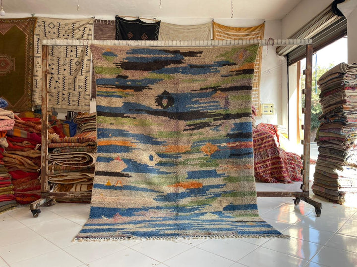 Lifestyle shot of a colorful blue Moroccan rug with orange and cream accents in a natural setting.