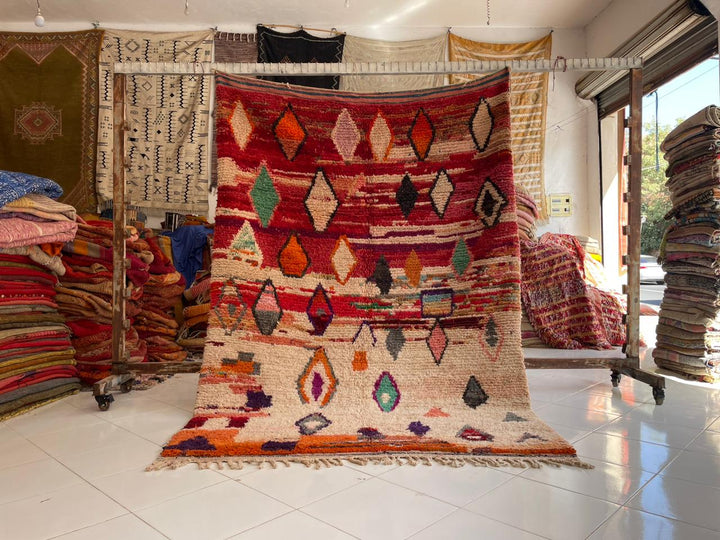 Lifestyle shot of a colorful red Moroccan rug with geometric patterns in a natural setting.