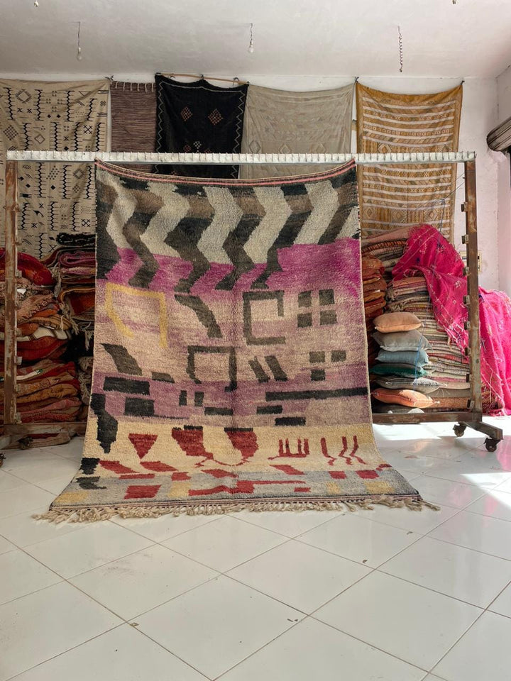 Lifestyle shot of a vintage Moroccan rug featuring tribal patterns in pink, red, and beige.