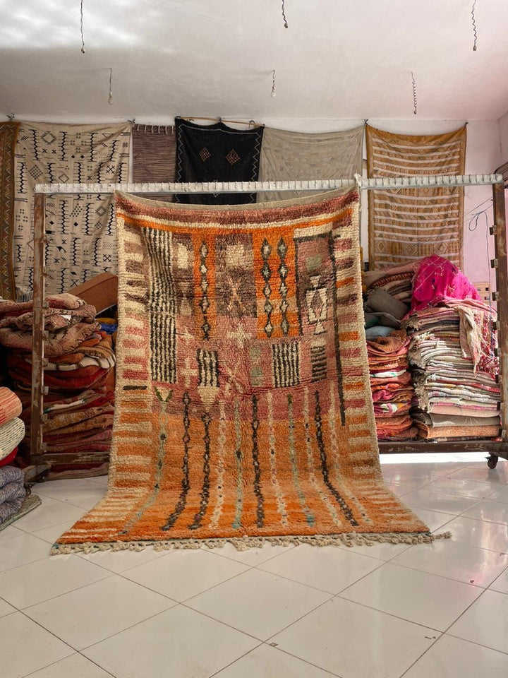 Lifestyle shot of a vintage Moroccan rug featuring tribal patterns in orange and black.