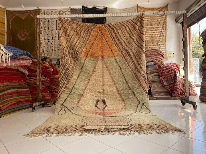 Lifestyle shot of a vintage Moroccan rug featuring geometric patterns in beige, orange, and green.