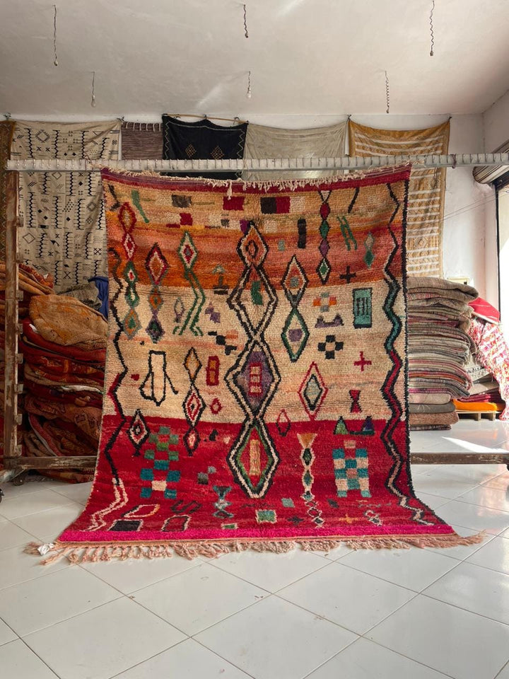 Lifestyle shot of a vintage Moroccan rug featuring intricate patterns in red, beige, and green.