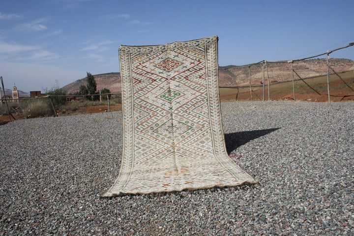Lifestyle shot of a vintage kilim rug with geometric patterns in beige, red, and green.