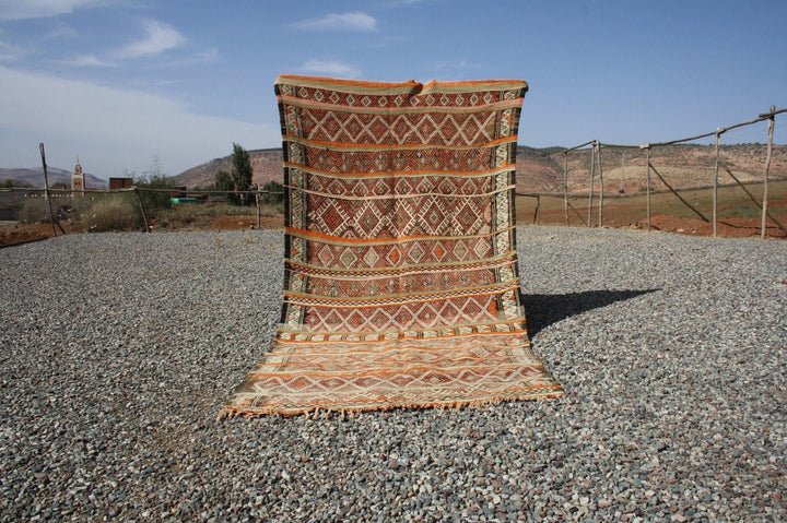 Lifestyle shot of a vintage kilim rug featuring geometric patterns in brown and orange.