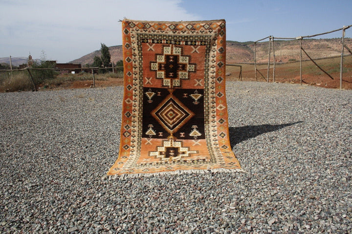 Lifestyle shot of a vintage kilim rug featuring geometric patterns in orange, black, and cream.