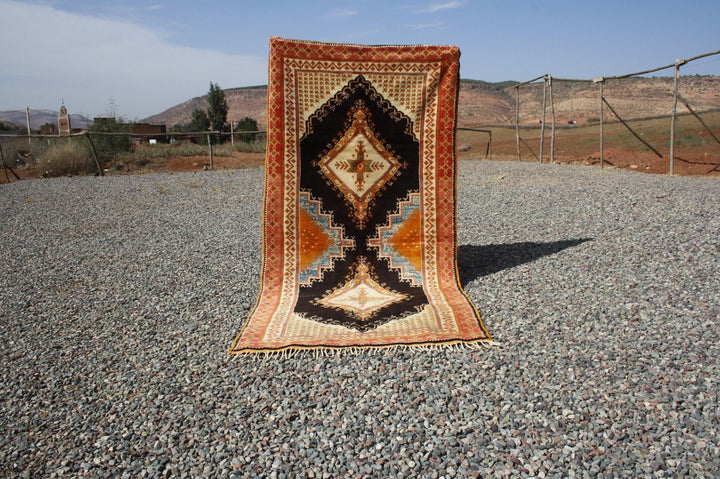 Lifestyle shot of a vintage kilim rug featuring geometric patterns in orange, black, and beige.