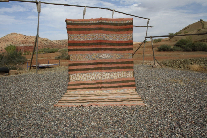 Lifestyle shot of a vintage kilim rug featuring a striped pattern in brown, orange, and beige.