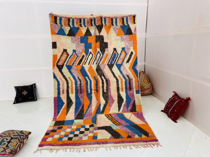 Lifestyle shot of a vintage Moroccan rug featuring abstract patterns in orange and blue.