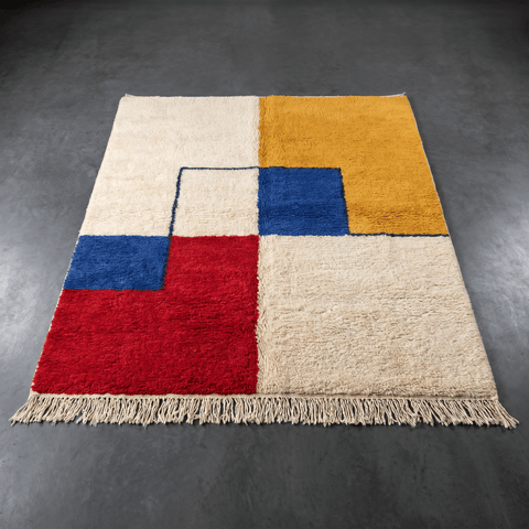 Lifestyle view of an abstract geometric rug showcasing beige, yellow, blue, and red colors with fringe detailing.