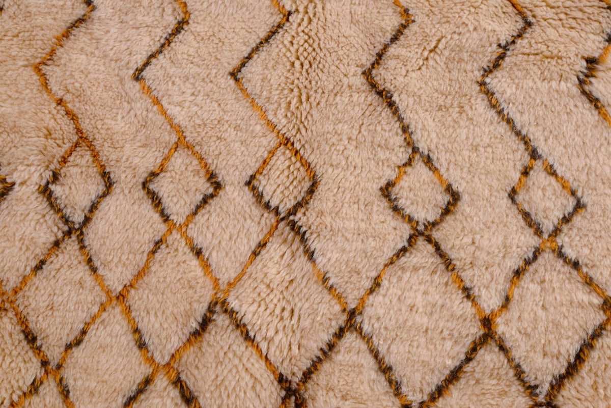 Close-up detail of the beige, brown, and orange geometric Moroccan rug with zigzag patterns and diamond shapes.