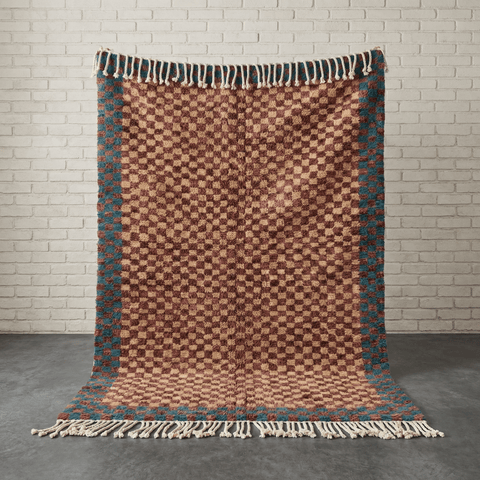 Front view of the burgundy checkered rug with fringe edges in a studio setting.