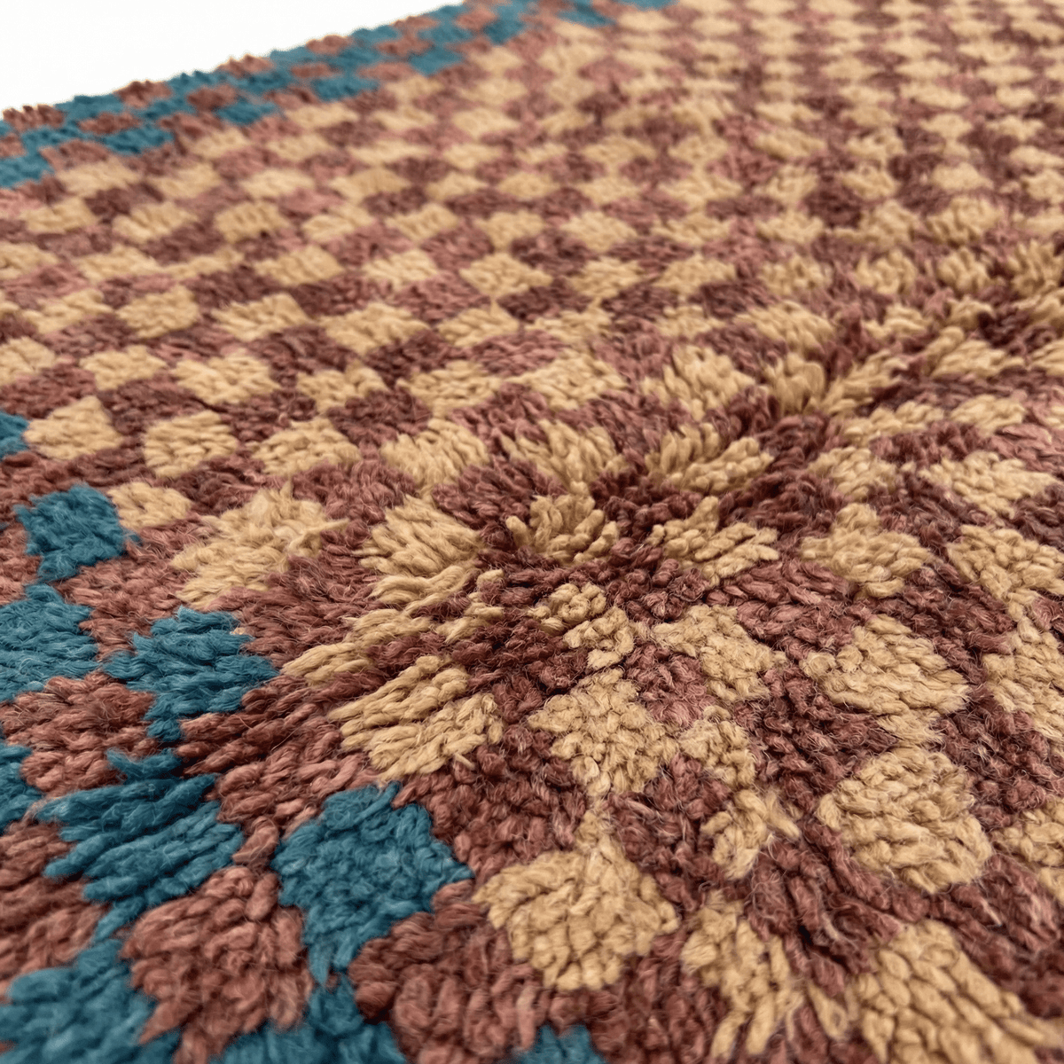 Detail close-up of the textured surface and fringe edges of the burgundy checkered rug.
