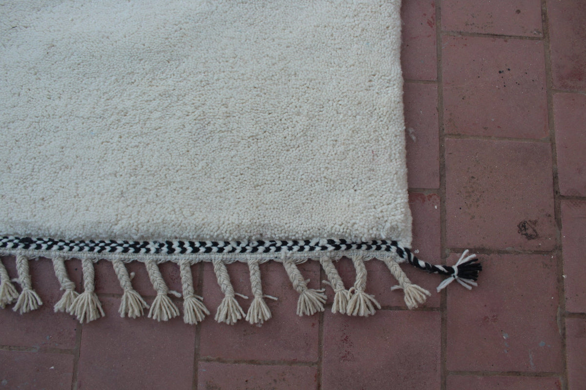 Detail shot of a Moroccan Beni Ourain rug showing fringe detail and a white background.