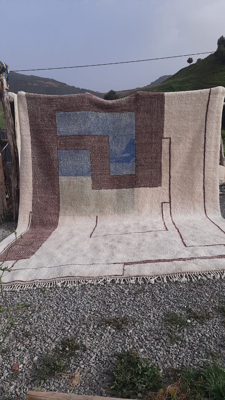 Lifestyle shot of a black and cream abstract Moroccan rug with geometric patterns on a natural background.