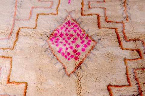 Close-up detail of a beige and pink Beni Ourain rug featuring a central motif and handcrafted details.