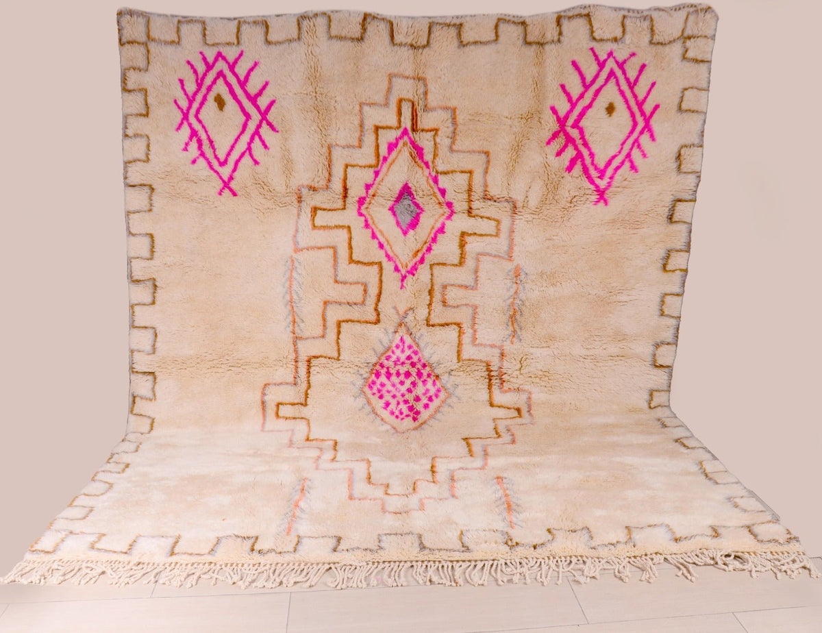 Detail shot of a beige and pink Beni Ourain rug featuring geometric patterns and fringe edges.
