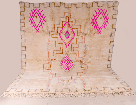 Detail shot of a beige and pink Beni Ourain rug featuring geometric patterns and fringe edges.