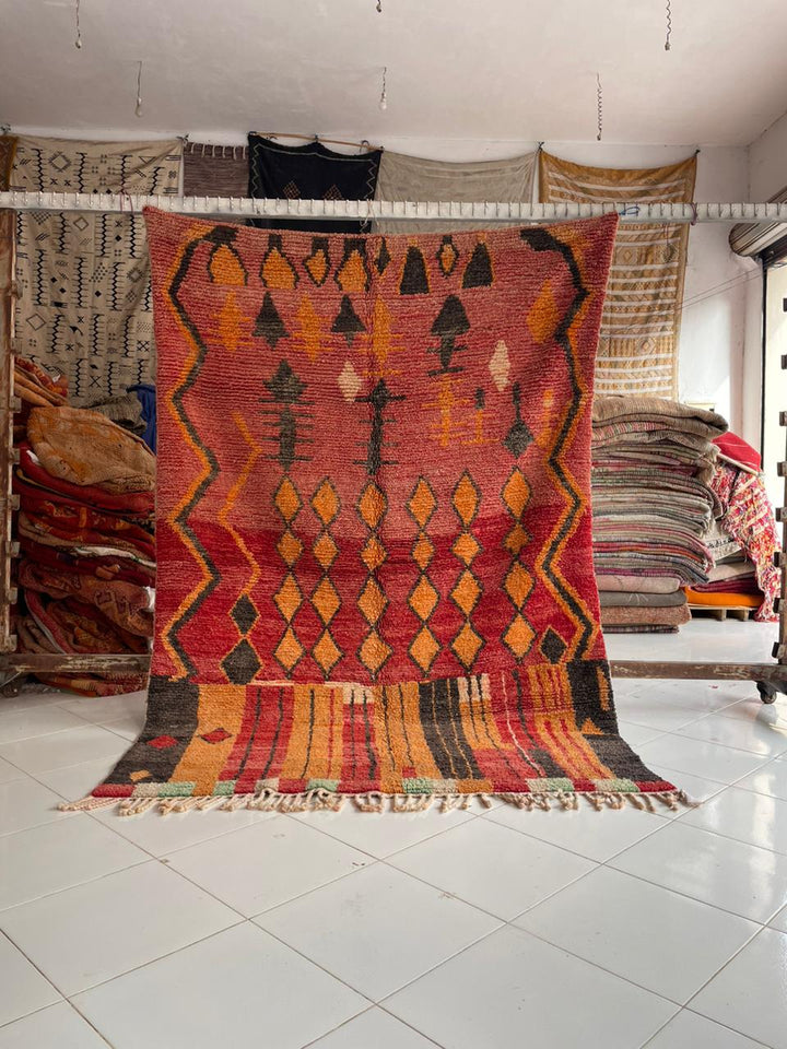 Front view of a vintage Moroccan rug featuring geometric patterns in red, orange, and black.