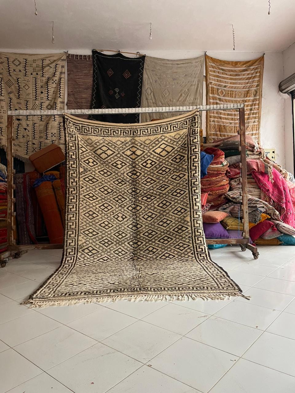Lifestyle shot of a beige and black Moroccan rug with traditional patterns and fringed edges.