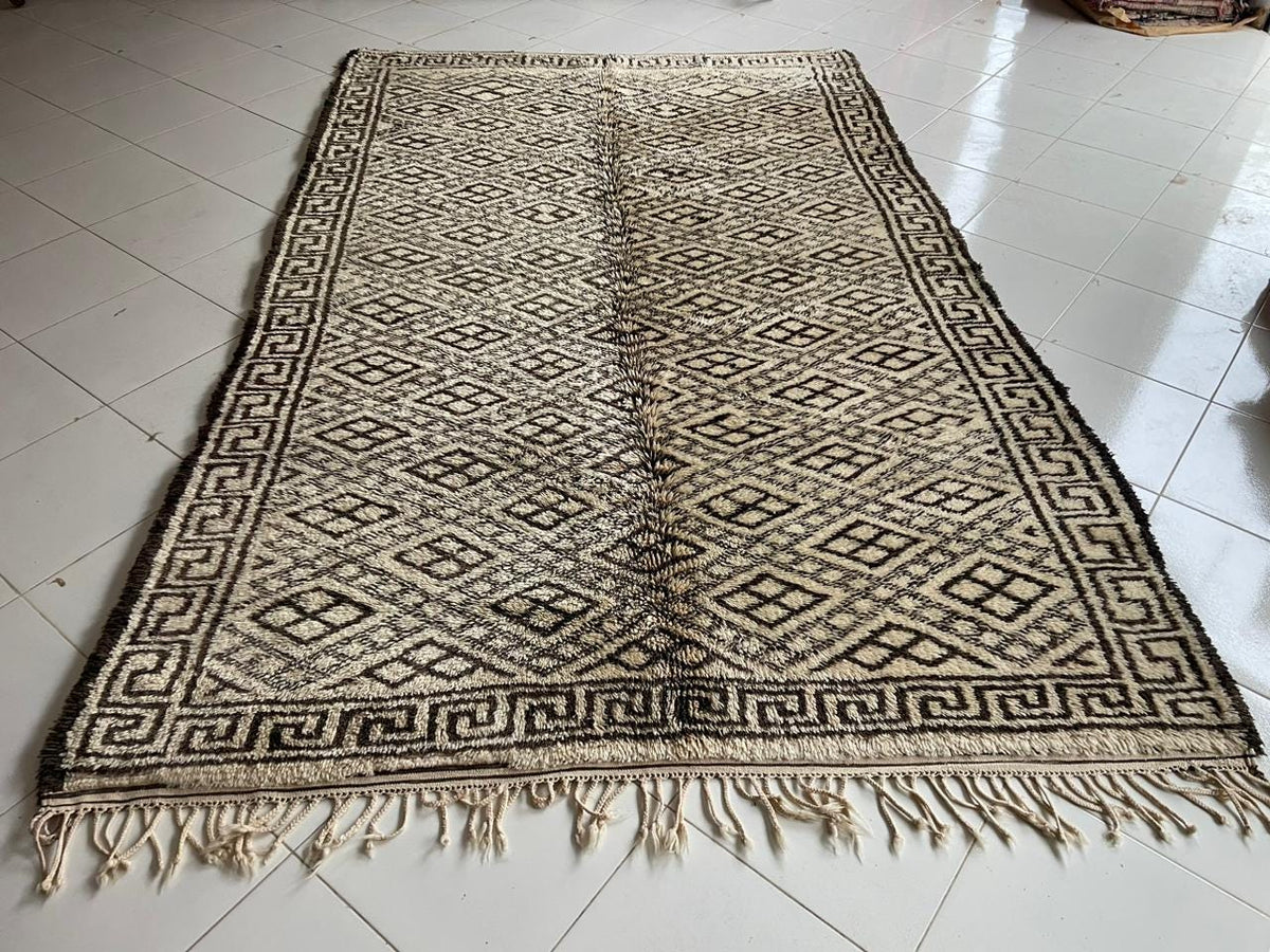 Front view of a large beige and black Moroccan rug featuring fringed edges.