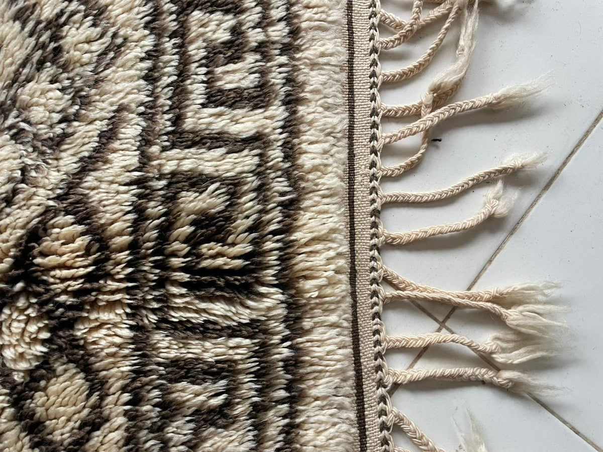Close-up detail of a beige and black Moroccan rug featuring geometric patterns and fringed edges.