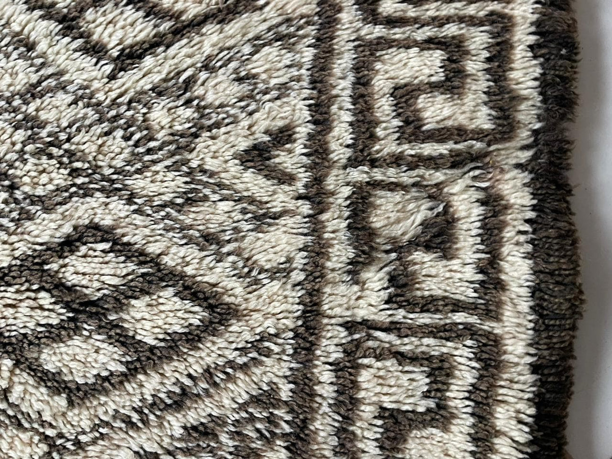 Close-up detail of a vintage Moroccan rug in black and cream showcasing an intricate design and fringe edge.