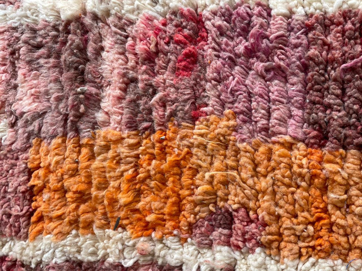 Detail view of a vintage Moroccan rug featuring orange, pink, and cream colors.