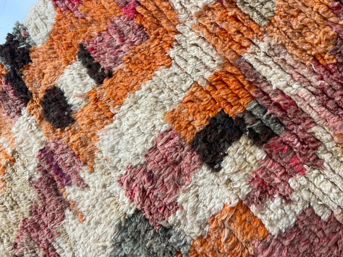 Detail close-up of a vintage Moroccan rug showcasing colorful patterns in orange, green, and white.